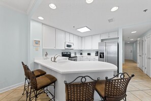 Une cuisine moderne avec des meubles blancs, un îlot central doté de tabourets et des appareils électroménagers en acier inoxydable.