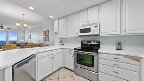 A modern kitchen with white cabinetry, stainless steel appliances, and a view to the outside. - Beautiful Beach Front Condo With Breathtaking Views (Orange Beach)