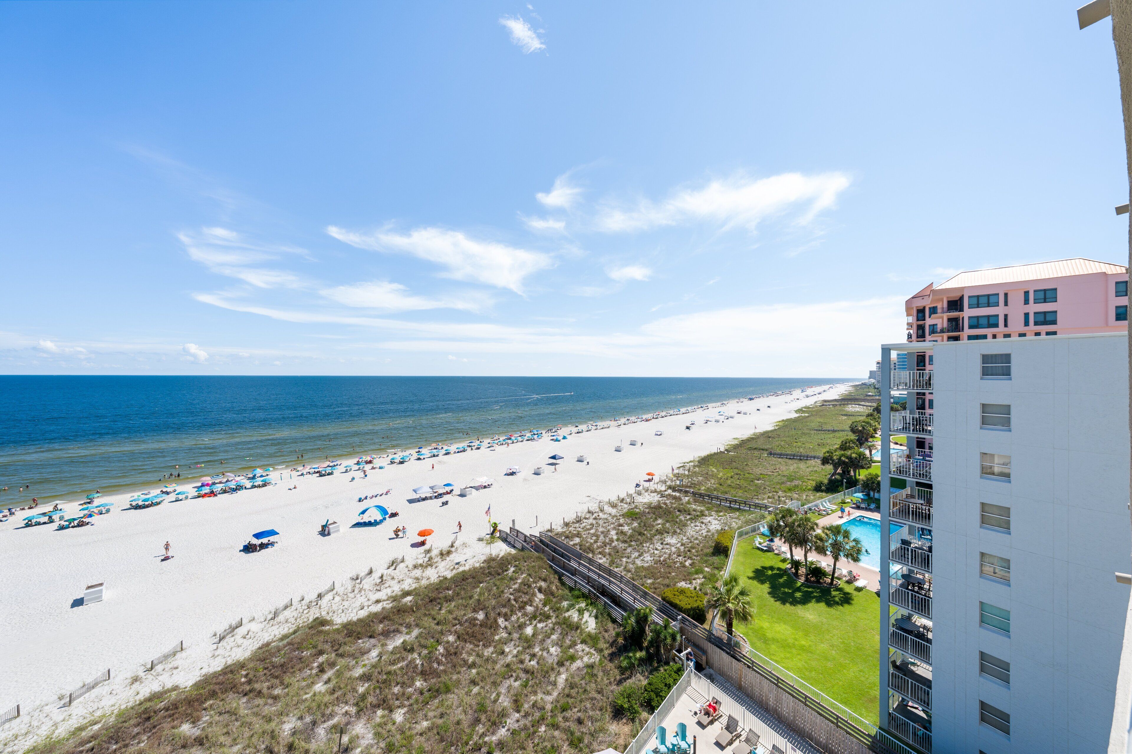A beach with a view of the ocean, a hotel building, and a pool area.