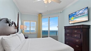 A hotel room with a bed, a dresser, a television displaying 'Gold Star Vacation Rentals', and a view of the ocean through a sliding door. - Beautiful Beach Front Condo With Breathtaking Views (Orange Beach)