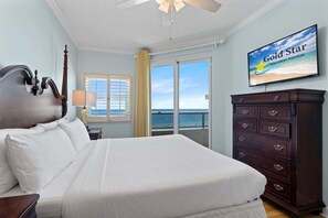 A hotel room with a bed, a dresser, a television displaying 'Gold Star Vacation Rentals', and a view of the ocean through a sliding door. - Beautiful Beach Front Condo With Breathtaking Views (Orange Beach)