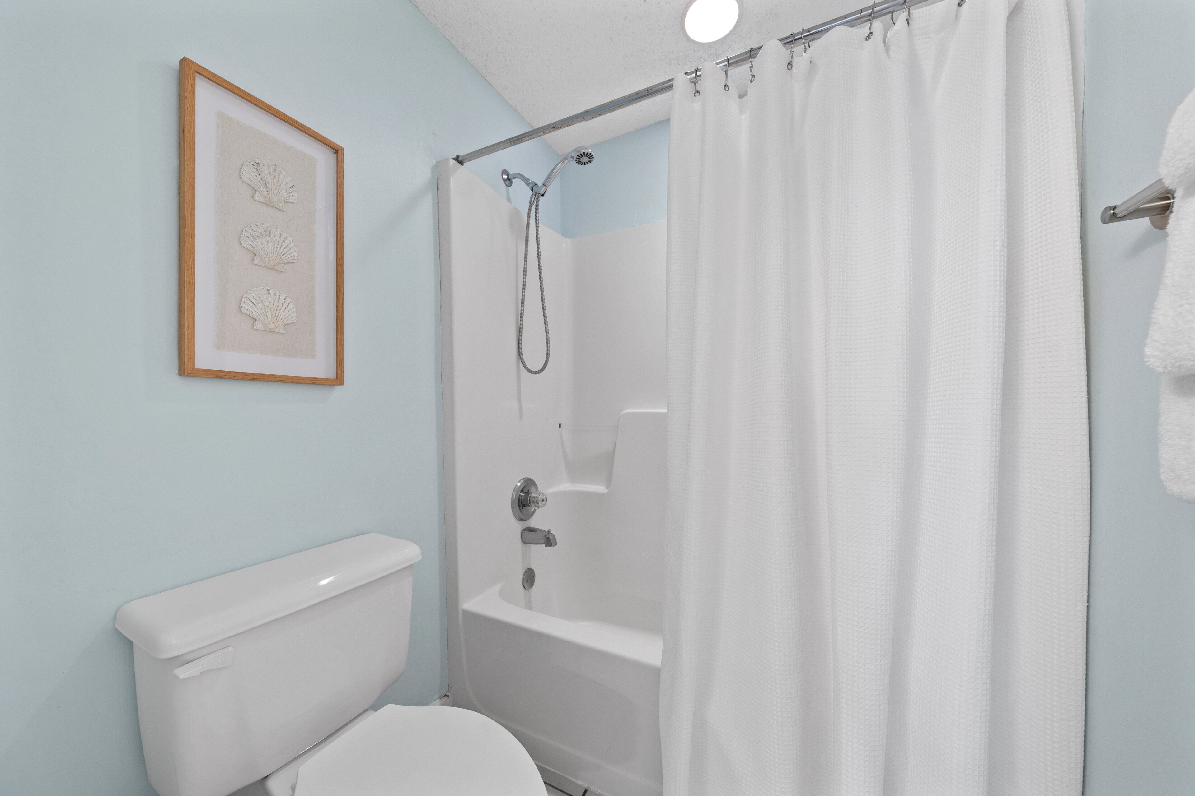 A bathroom with a toilet, a shower with a curtain, and a framed picture on the wall.
