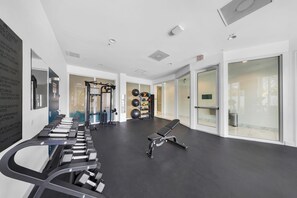 Ein Fitnessraum mit Trainingsgeräten, einer Bank und einer Wand mit Regeln.