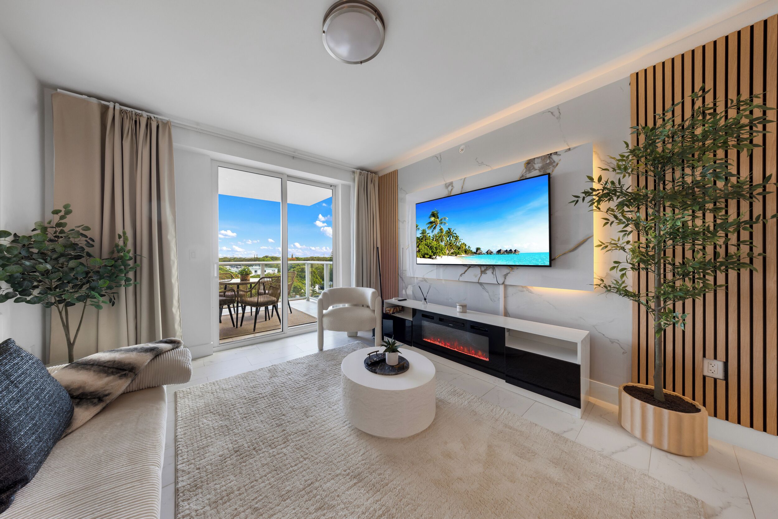 A modern living room with a flat-screen TV, a fireplace, and a balcony with outdoor furniture.