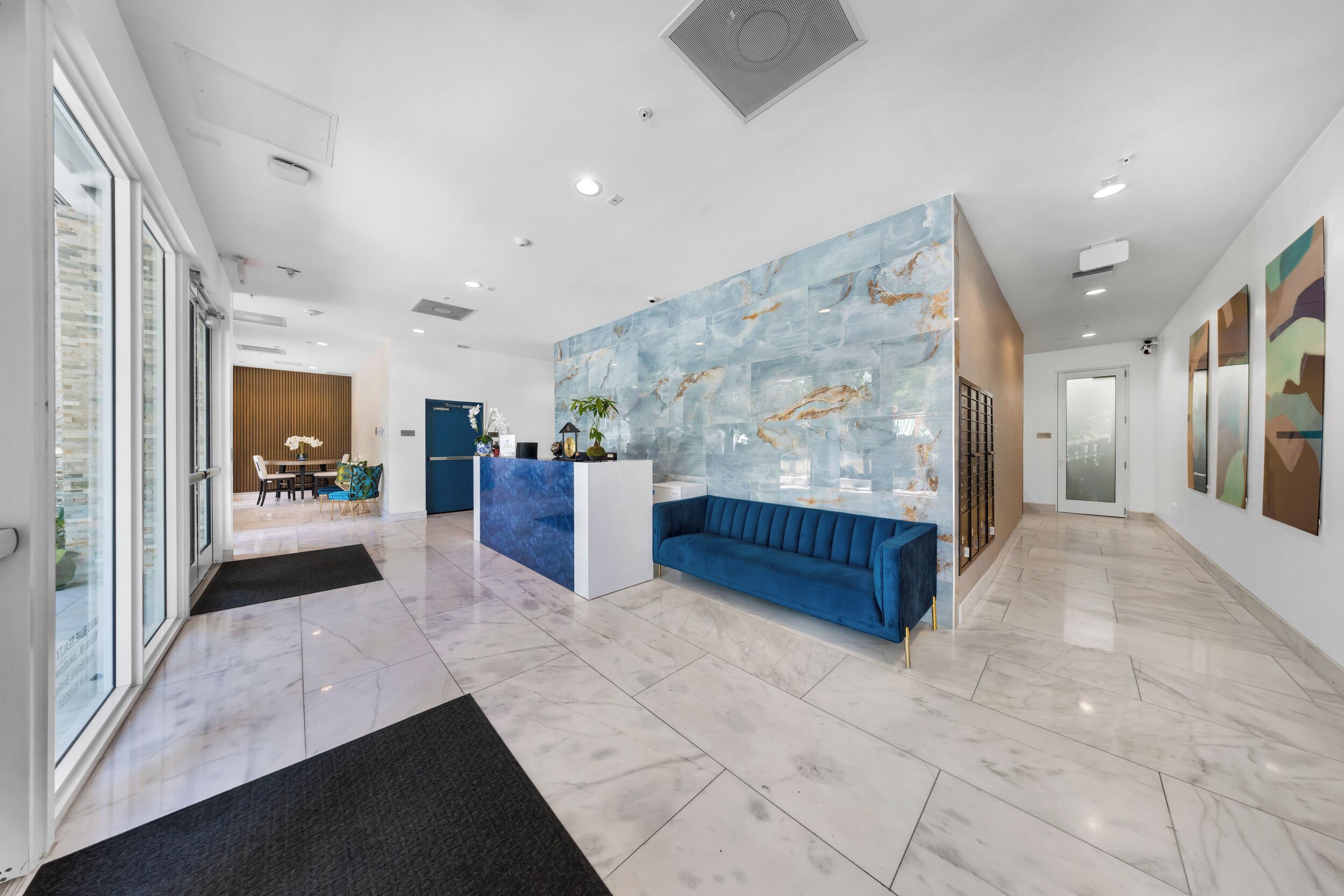 A modern lobby with a reception desk, a blue sofa, and a marble floor.