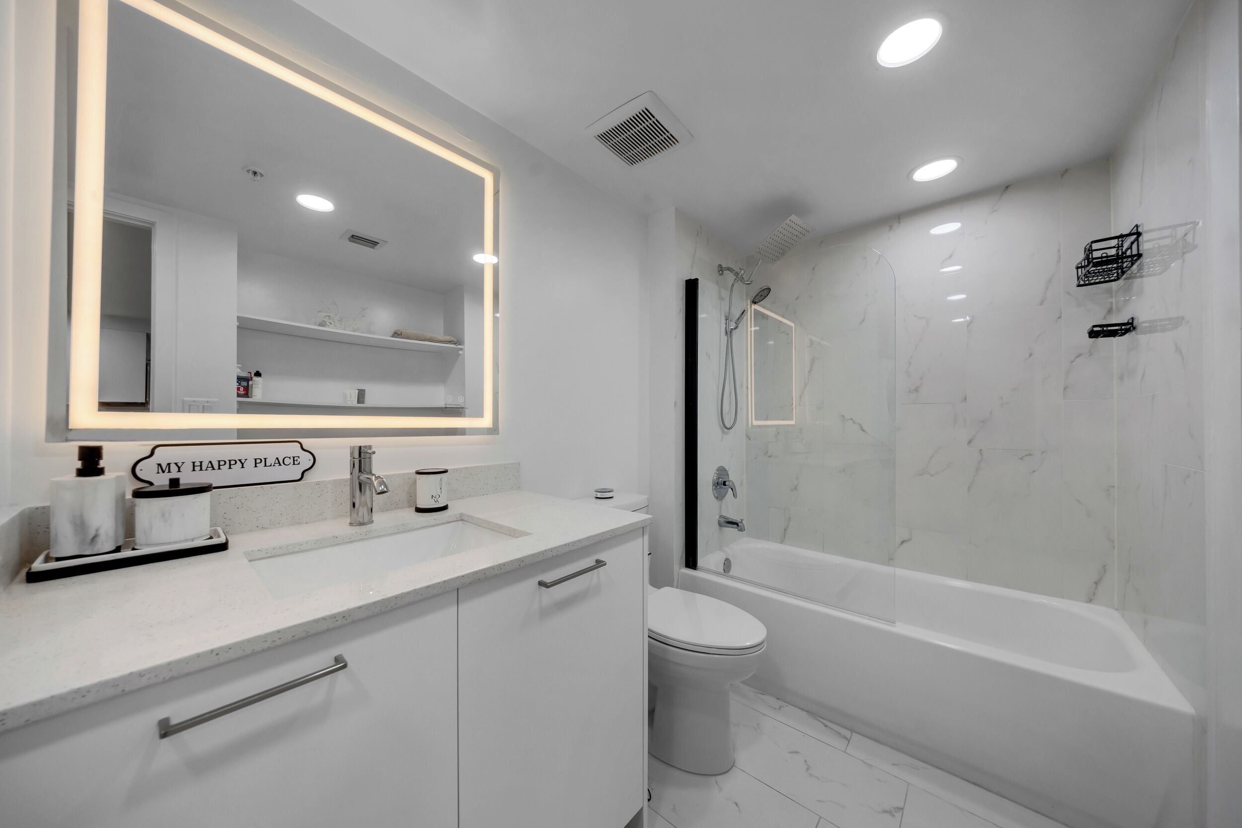 A modern bathroom with a large mirror, a bathtub, and a toilet.