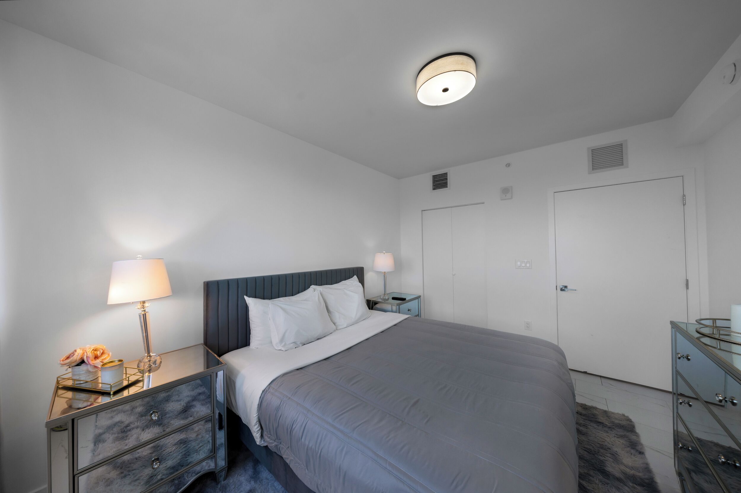 A hotel room with a bed, bedside tables, lamps, a wardrobe, and a ceiling light fixture.