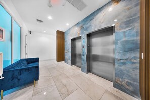 Eine moderne Lobby mit einem blauen Sofa, Marmorwänden und zwei Aufzügen.