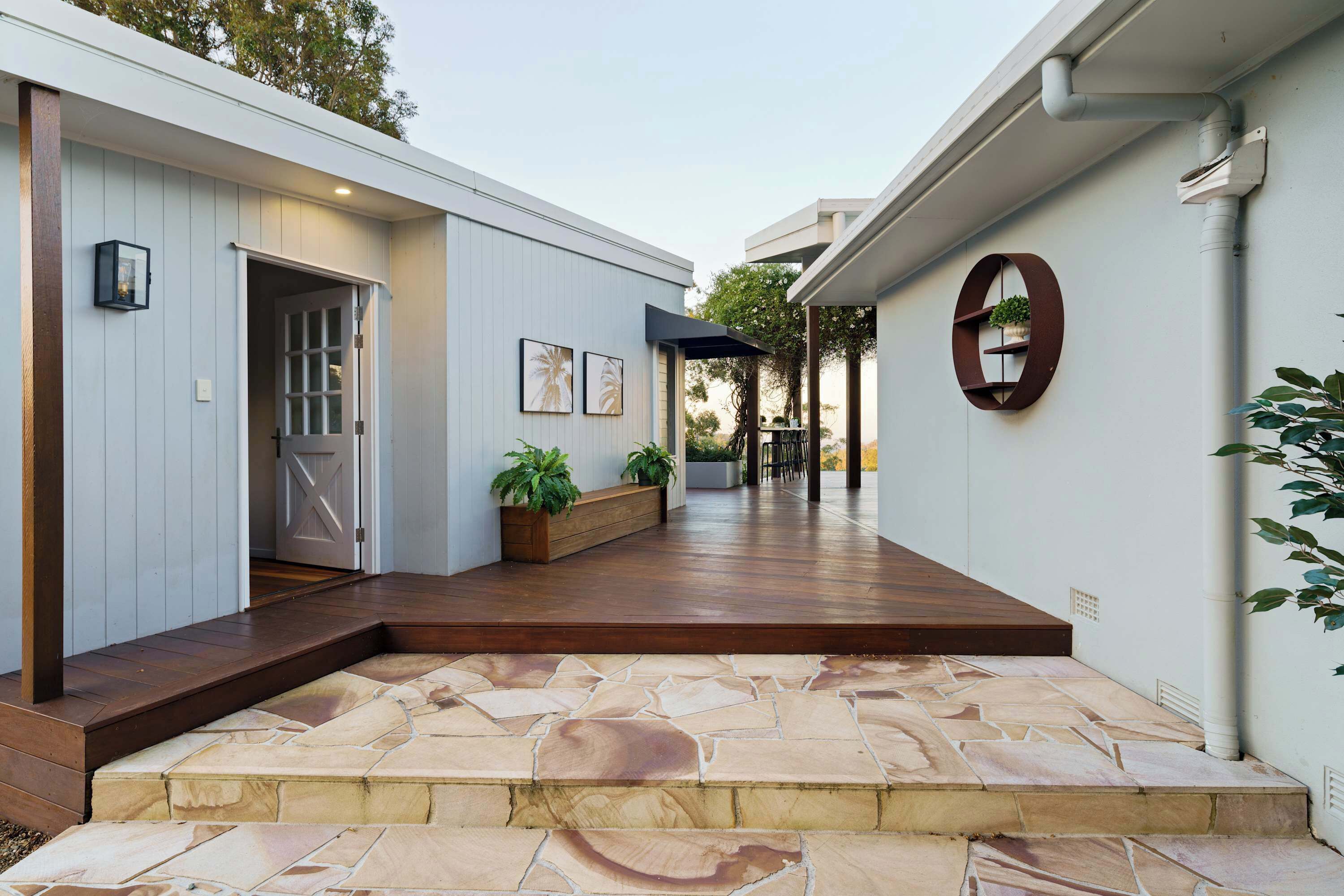 A modern building with a stone-tiled entrance, wooden benches, and a wall-mounted shelf with plants.