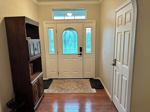 A hallway with a wooden floor, a rug, a door with glass panels, and a cabinet.