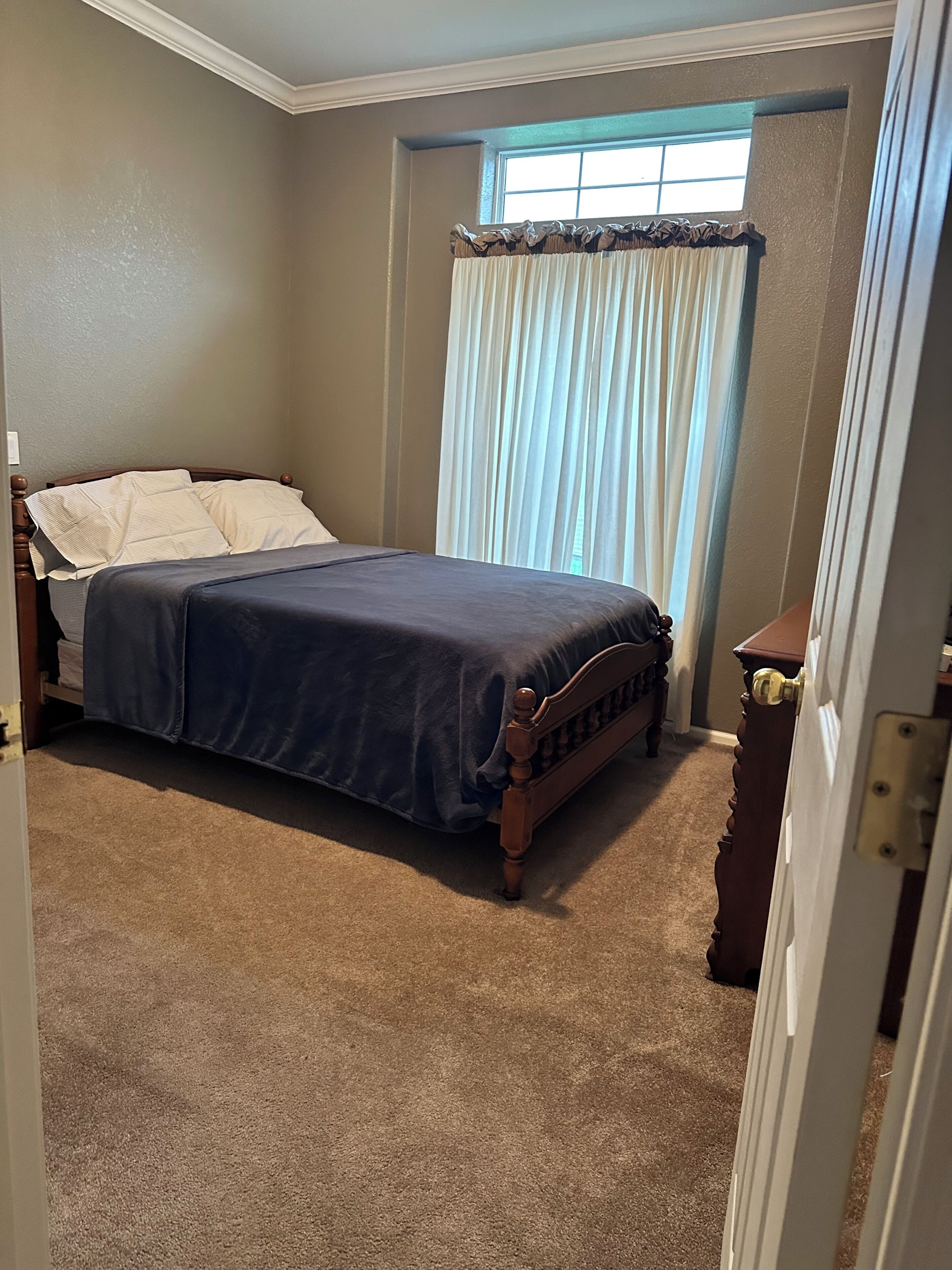 A bedroom with a bed, a window with curtains, a door, and a carpeted floor.