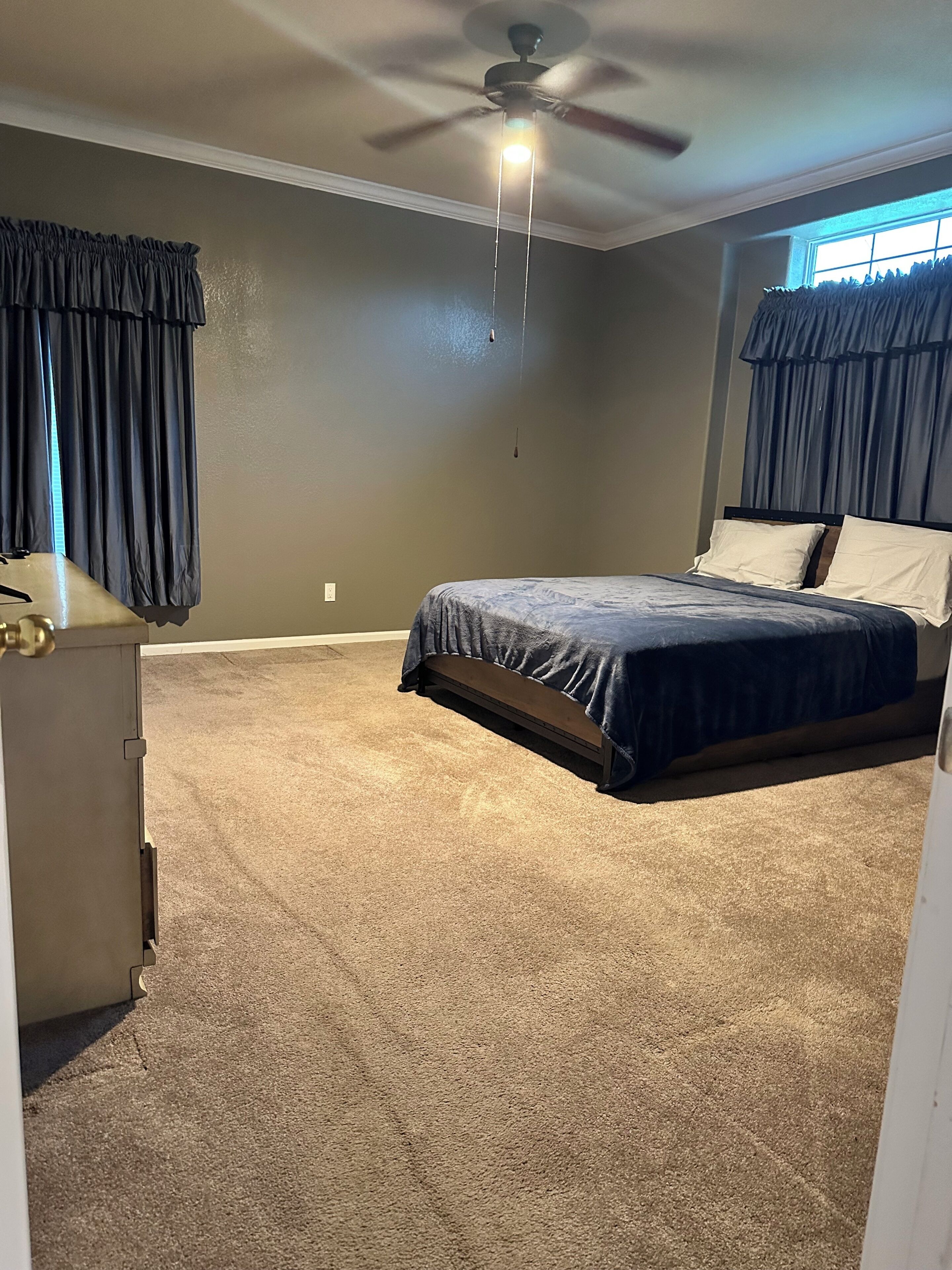 A bedroom with a bed, a ceiling fan, and a window with curtains.