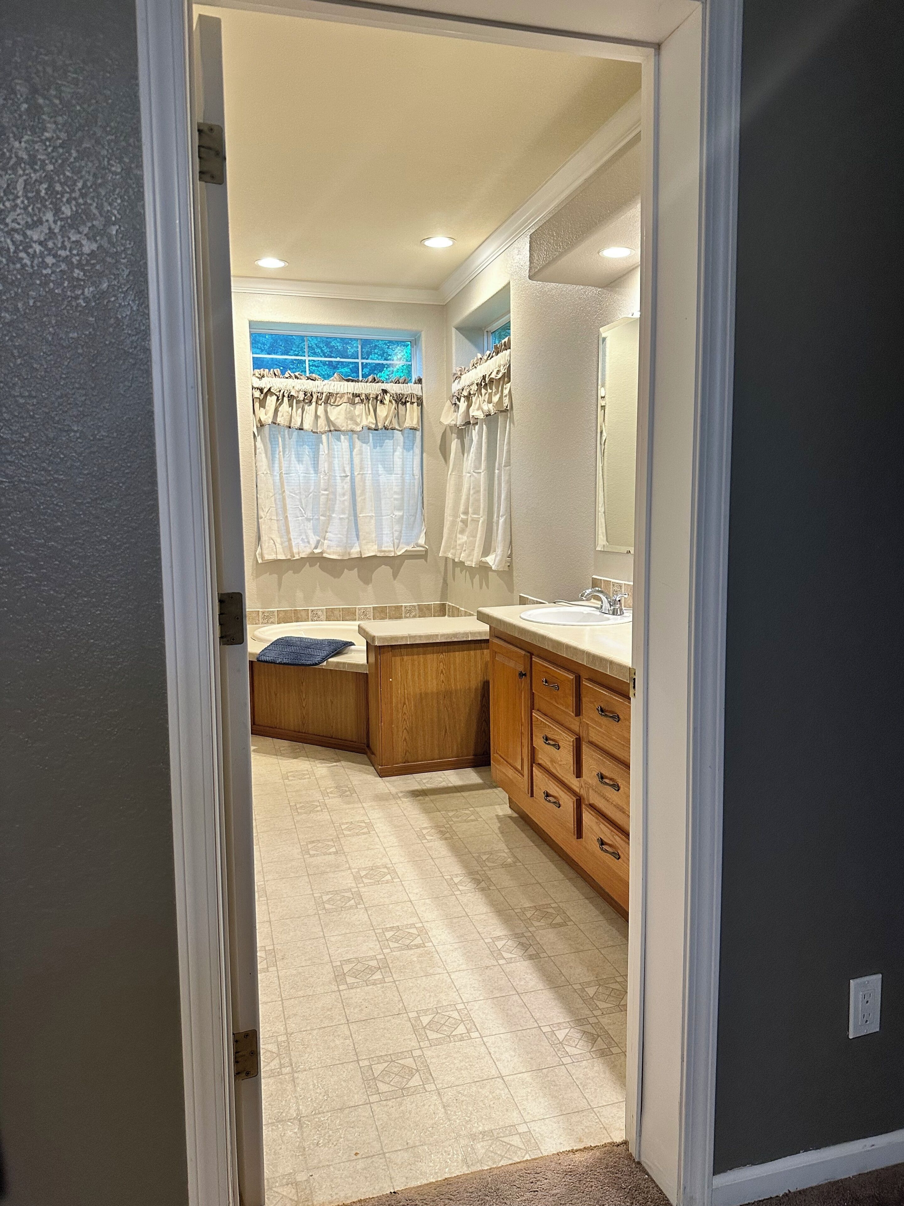 Baño con lavamanos, tocador y ventana con cortinas.