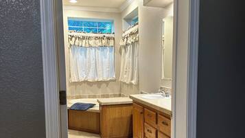 Baño con lavamanos, tocador y ventana con cortinas.