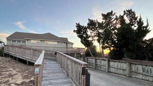 En træterrasse der fører til et hus med en indhegnet have og træer.