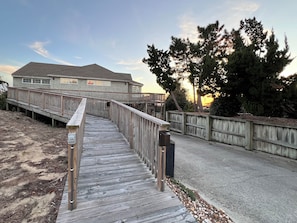 A wooden deck leading to a house with a fenced yard and trees. - Oceanside resort, hot tub, pool, walk to beach, tennis, amazing sunset views (Kitty Hawk)