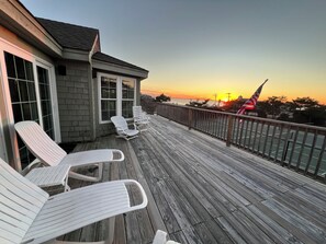 A wooden deck with white lounge chairs and a view of the sunset over the water. - Oceanside resort, hot tub, pool, walk to beach, tennis, amazing sunset views (Kitty Hawk)