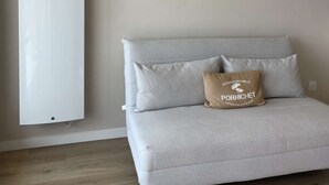 A minimalist room with a grey sofa, a single pillow with text, and a white air conditioning unit. - PORNICHET - FACE MER (PORNICHET)