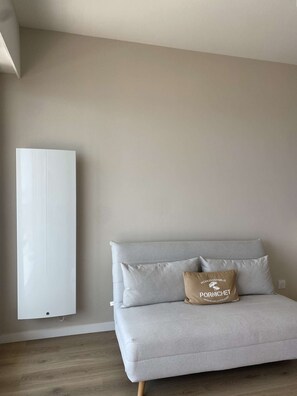 Ein schlichter Raum mit einem grauen Sofa, einem Kissen mit Aufdruck und einer weißen Klimaanlage.