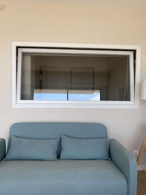 A room with a large window, a light blue sofa, and a wall-mounted light fixture. - PORNICHET - FACE MER (PORNICHET)