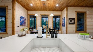 A kitchen with a large island, wooden ceiling, and artwork on the walls. - Record Time | Pool, Hot Tub, Game Room, Sleeps 15 (Broken Bow)