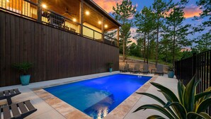 A swimming pool with a wooden deck, surrounded by potted plants and a wooden fence. - Record Time | Pool, Hot Tub, Game Room, Sleeps 15 (Broken Bow)