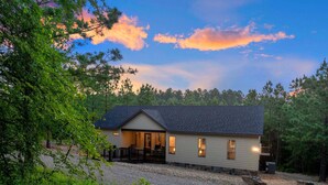 A two-story house with a porch, surrounded by trees and a gravel driveway. - Record Time | Pool, Hot Tub, Game Room, Sleeps 15 (Broken Bow)