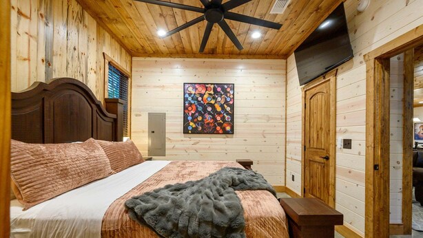 A bedroom with a wooden ceiling fan, a bed with a headboard, a wall-mounted painting, and a door leading to another room. - Record Time | Pool, Hot Tub, Game Room, Sleeps 15 (Broken Bow)