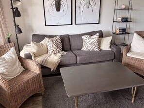 Un salon avec un canapé gris, deux fauteuils, une table basse, un lampadaire et une bibliothèque.