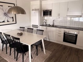 Una cocina moderna con armarios blancos, horno de acero inoxidable y comedor con mesa blanca y sillas negras.
