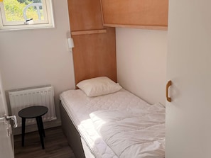A small, single-bed room with a wooden headboard, a small table, and a radiator.
