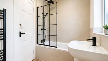 Un baño con cabina de ducha, lavamanos y una puerta con perchero.