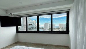 A bedroom with a large window, a bed, and a flat-screen TV mounted on the wall. - TOP/2BR/Home Away From Home/Ocean views/Balcony/HZ (Cancún)