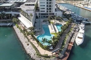 A hotel with a pool, a marina with boats, and a waterfront view. - TOP · Puerto Cancún · Café y balcón frente a yates (Cancún)