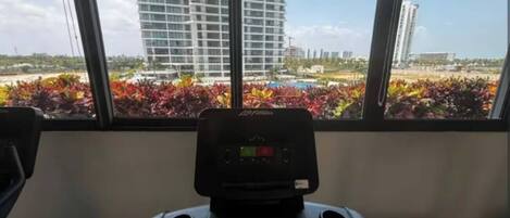 A treadmill with a digital display, positioned in front of a window with a view of a building and colorful plants.