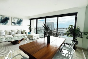 A modern living room with a large dining table, a sofa set, and a view of the city through large windows. - TOP · Puerto Cancún · Café y balcón frente a yates (Cancún)