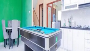 A pool table in a room with a green wall and a kitchen area with white cabinets. - Cozzy Villa Gardenia (batu)