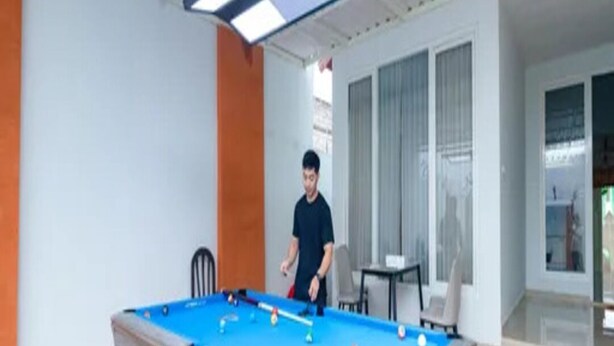 A pool table in a room with a modern design, including a ceiling light fixture and a view of the outdoors through a glass door. - Cozzy Villa Gardenia (batu)