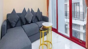 A modern living room with a grey sectional sofa, a small round table, and a large sliding glass door leading to an outdoor balcony. - Cozzy Villa Gardenia (batu)