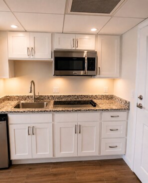 A kitchen with white cabinets, a stainless steel microwave, a granite countertop, and a dishwasher. - 15th Floor Riverfront Retreat - Walk to Downtown - Pool (Fort Myers)