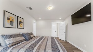 A bedroom with a large bed, a flat-screen TV mounted on the wall, and two framed artworks on the wall. - Unforgettable 4BD Oasis in West Texas (Midland)