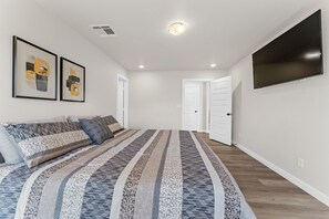 Quarto com uma cama grande, uma TV de tela plana na parede e duas obras de arte emolduradas na parede.