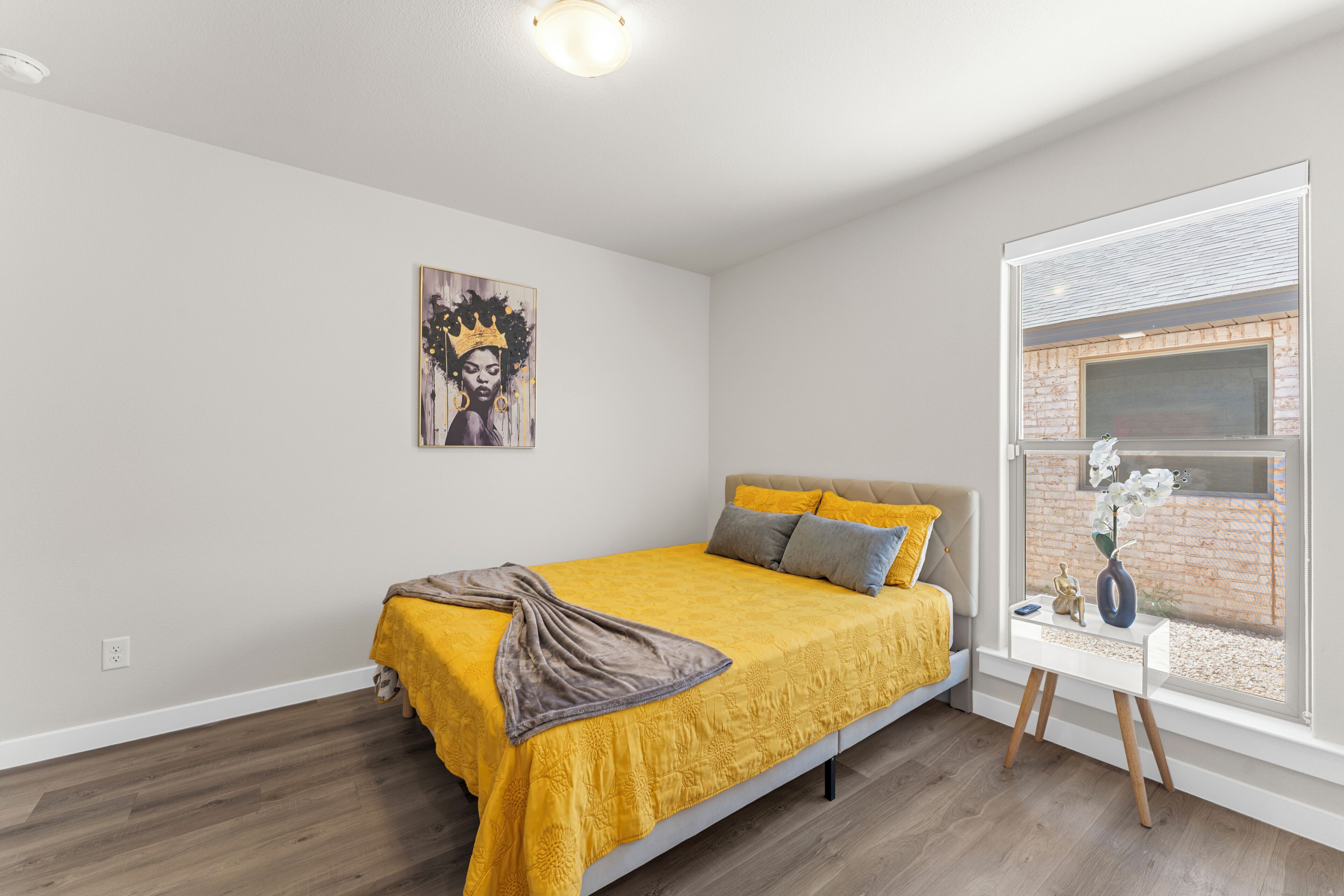 Une chambre à coucher avec un lit, une fenêtre donnant sur un mur de briques et un tableau accroché au mur.
