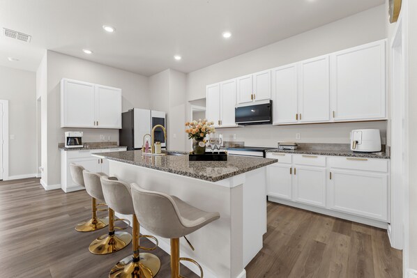 A modern kitchen with white cabinetry, a granite countertop, and gold bar stools. - Unforgettable 4BD Oasis in West Texas (Midland)