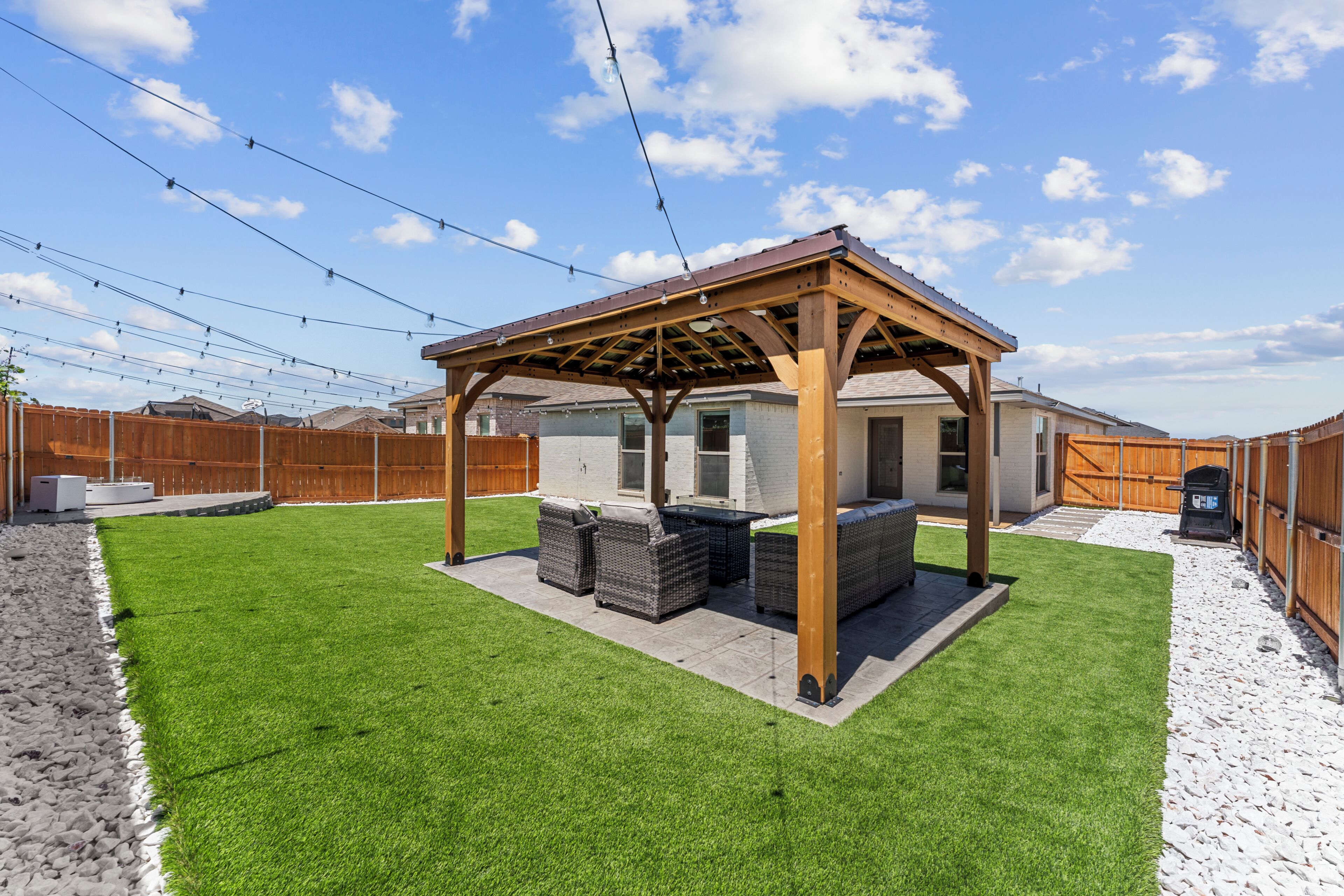 A backyard with a wooden pergola, outdoor seating, and a well-maintained lawn.