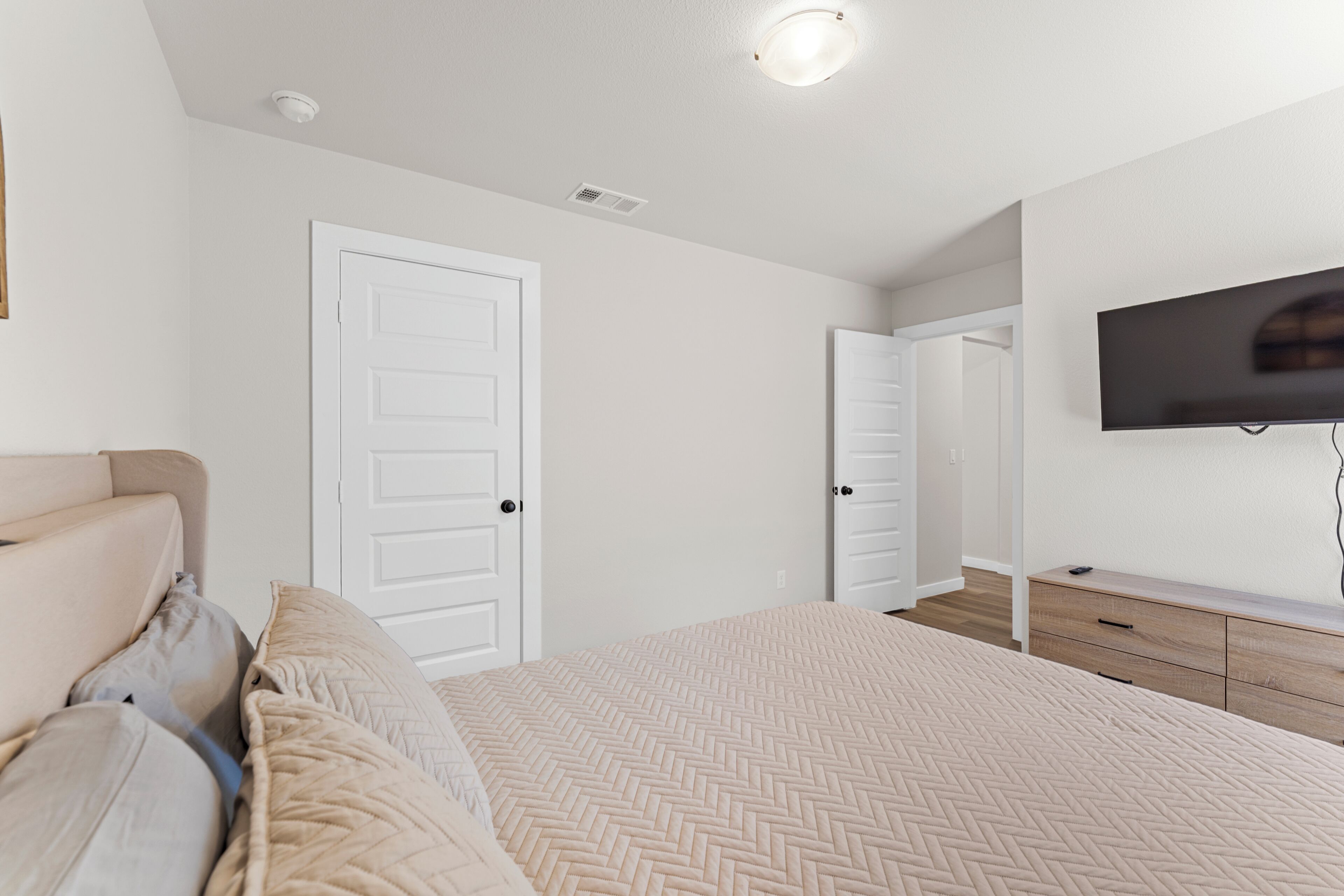 A bedroom with a bed, a TV mounted on the wall, and a door leading to another room.