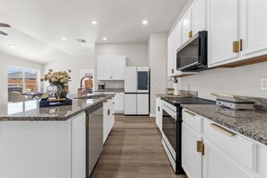A modern kitchen with white cabinetry, granite countertops, and stainless steel appliances. - Unforgettable 4BD Oasis in West Texas (Midland)