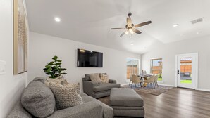 A spacious living room with a ceiling fan, a flat-screen TV, and a dining area with a table and chairs. - Unforgettable 4BD Oasis in West Texas (Midland)