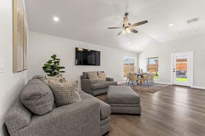 Uma sala de estar ampla com ventilador de teto, televisão de tela plana e área de jantar com mesa e cadeiras.