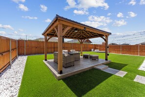 A wooden pergola with seating, surrounded by a wooden fence and a grassy lawn. - Unforgettable 4BD Oasis in West Texas (Midland)